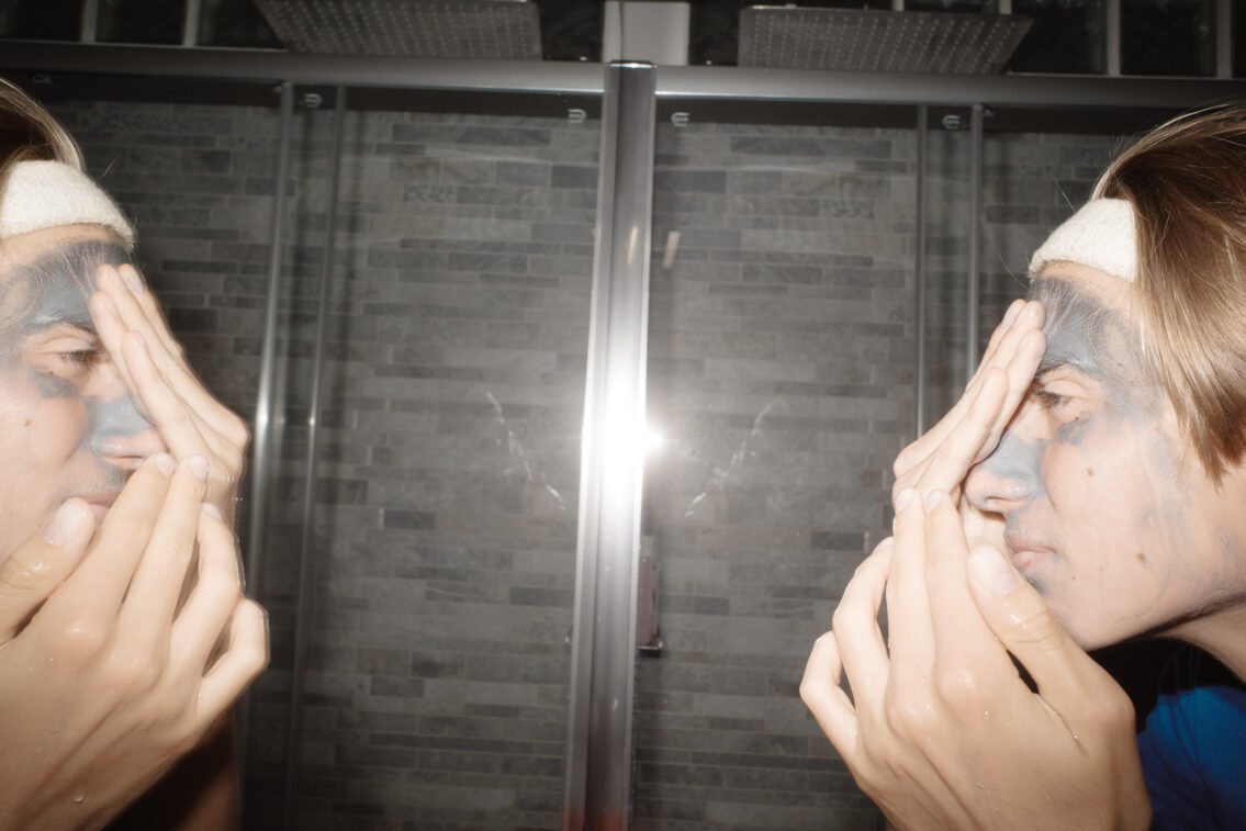 A teenage boy peeling off a face mask treatment, in a routine day, reflecting a slice of adolescent life.